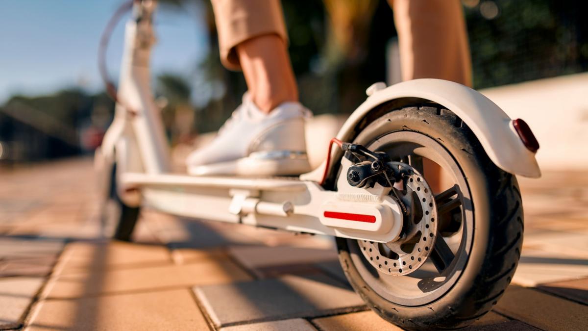 Close-up of a woman's feet on an electric scooter, focusing on the wheel in the foreground.