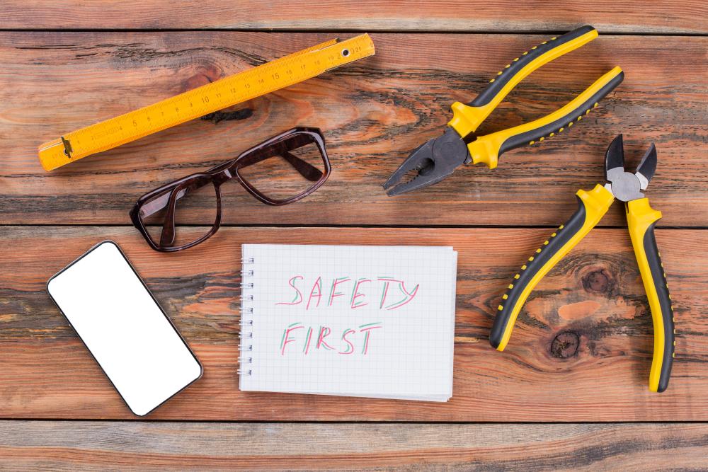 A top view image of various hand tools consist of pliers, nippers, ruler and a notebook that says Safety First on it written in marker.